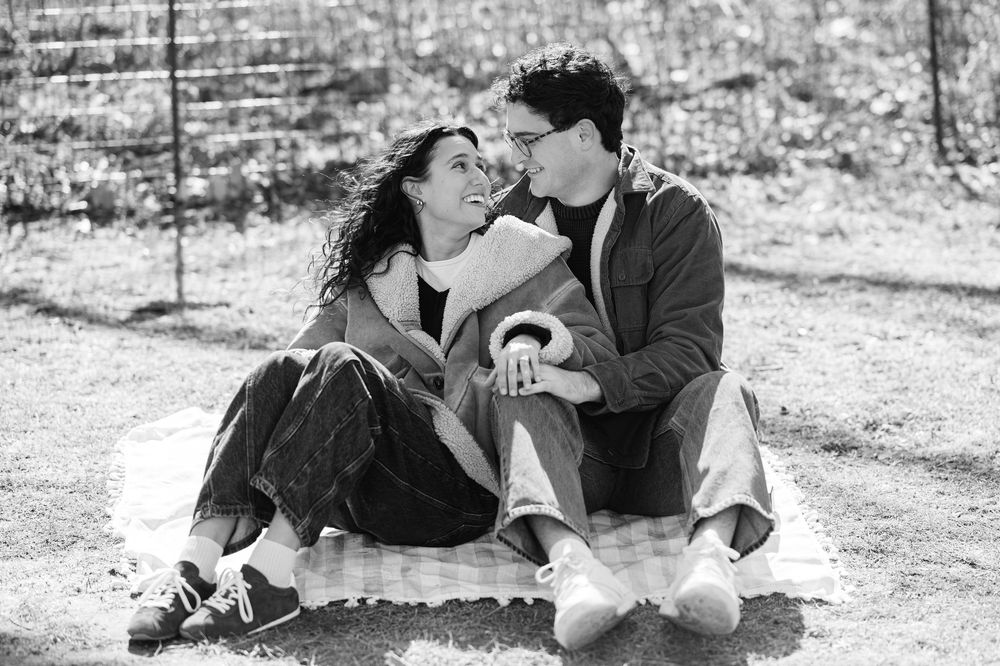 Black and white romantic photo showing a couple sitting together on a picnic blanket during a proposal session in Prospect Park.