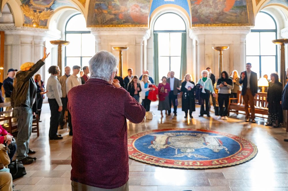 Visitors explore an ornate circular room with gilded details and painted ceiling in a historic palace or museum.