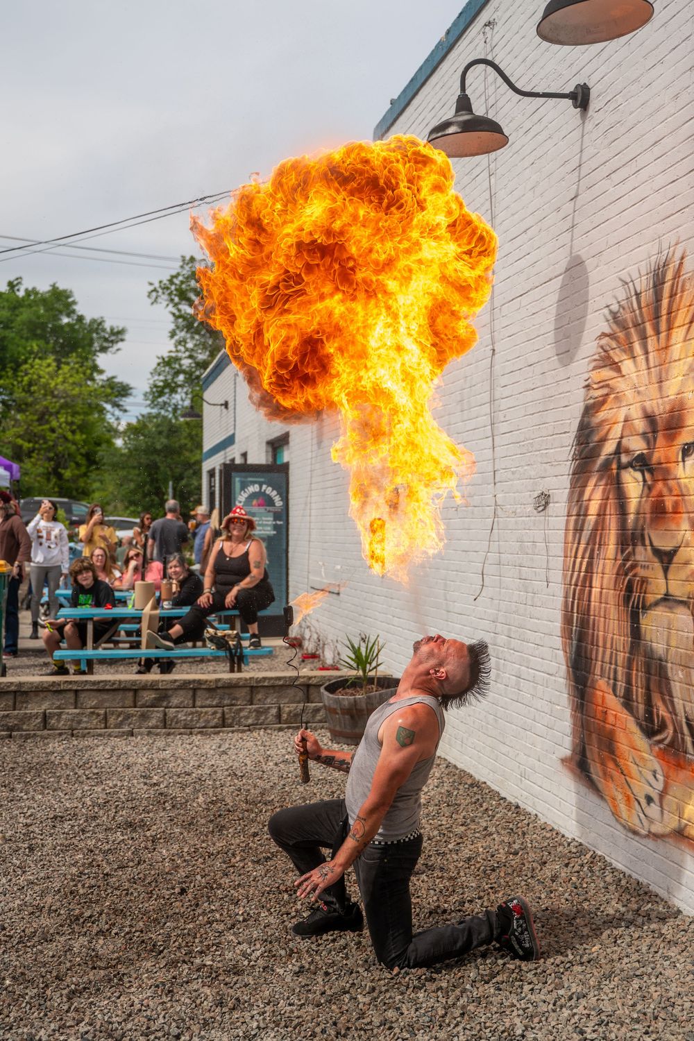 A fire breather performs a dramatic fire breathing display against a white wall with street art in a sequence of photos.