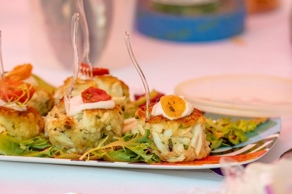 Elegant crab cakes garnished with sliced carrots and microgreens served on a white rectangular plate.