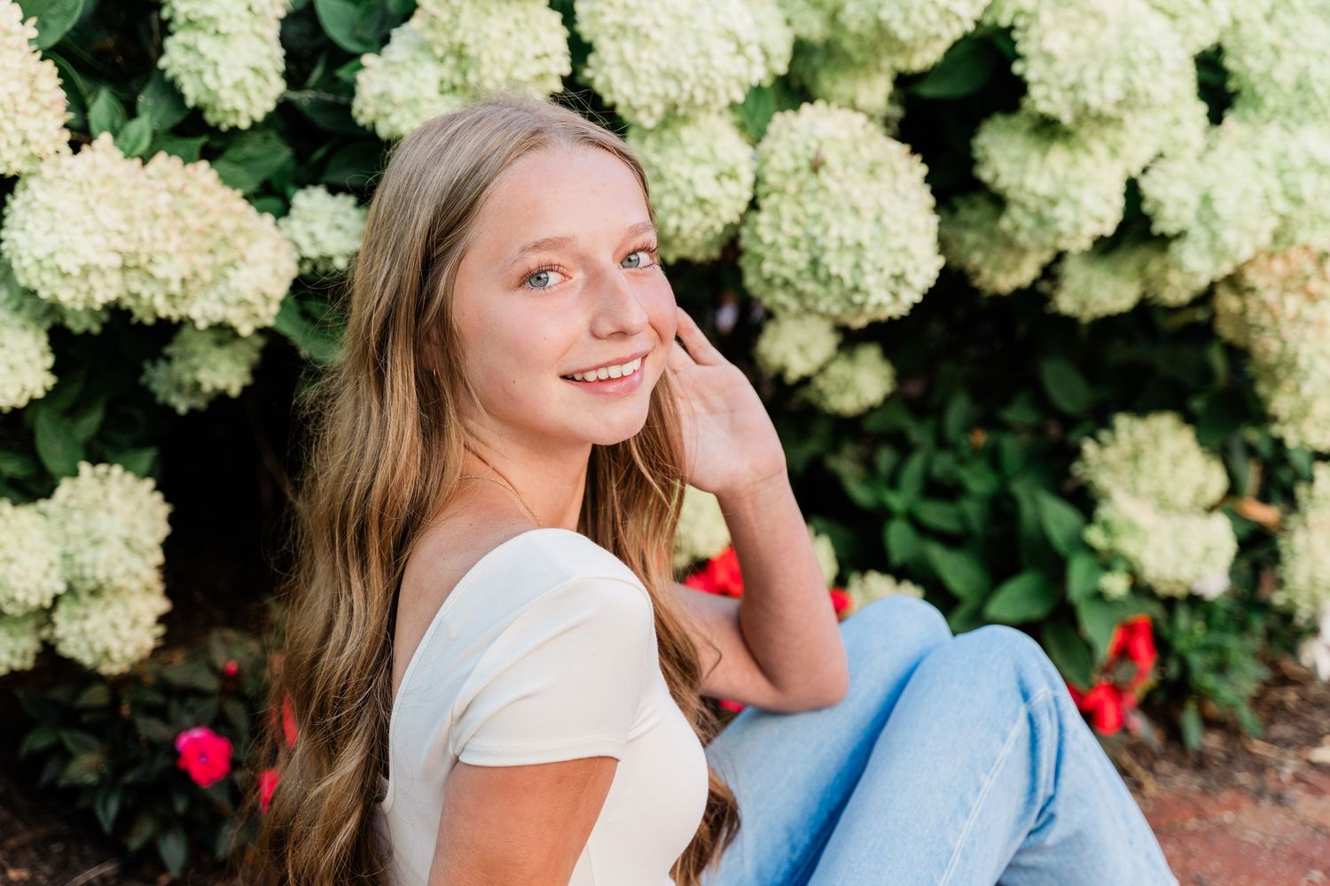 Toledo senior session with Perrysburg High School student sits and laughs in a garden with blooming white hydrangea bushes in the background
