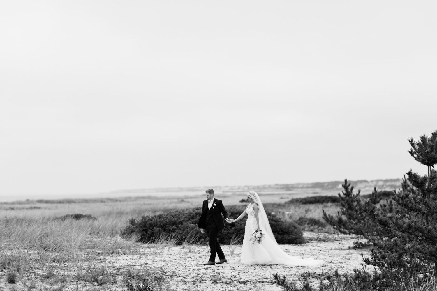 Silhouettes walking along beach shoreline in black and white photography.