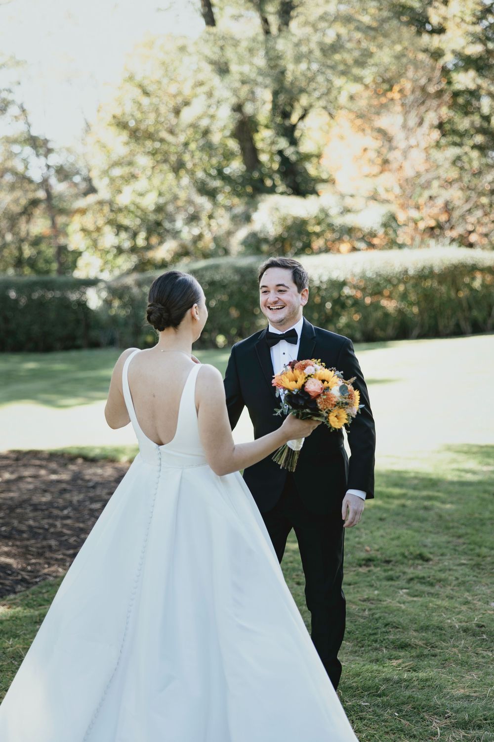 A romantic first look moment between newlyweds in a sunlit garden setting with autumn foliage in the background.