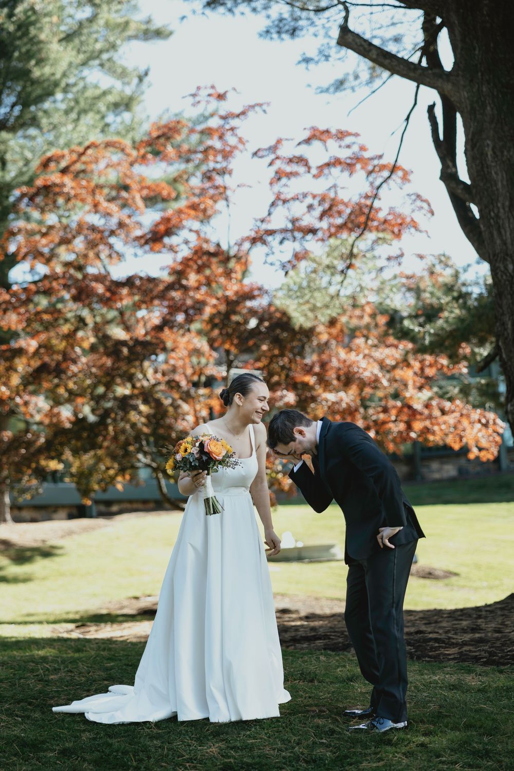 A couple shares a joyful moment outdoors under trees with autumn foliage.