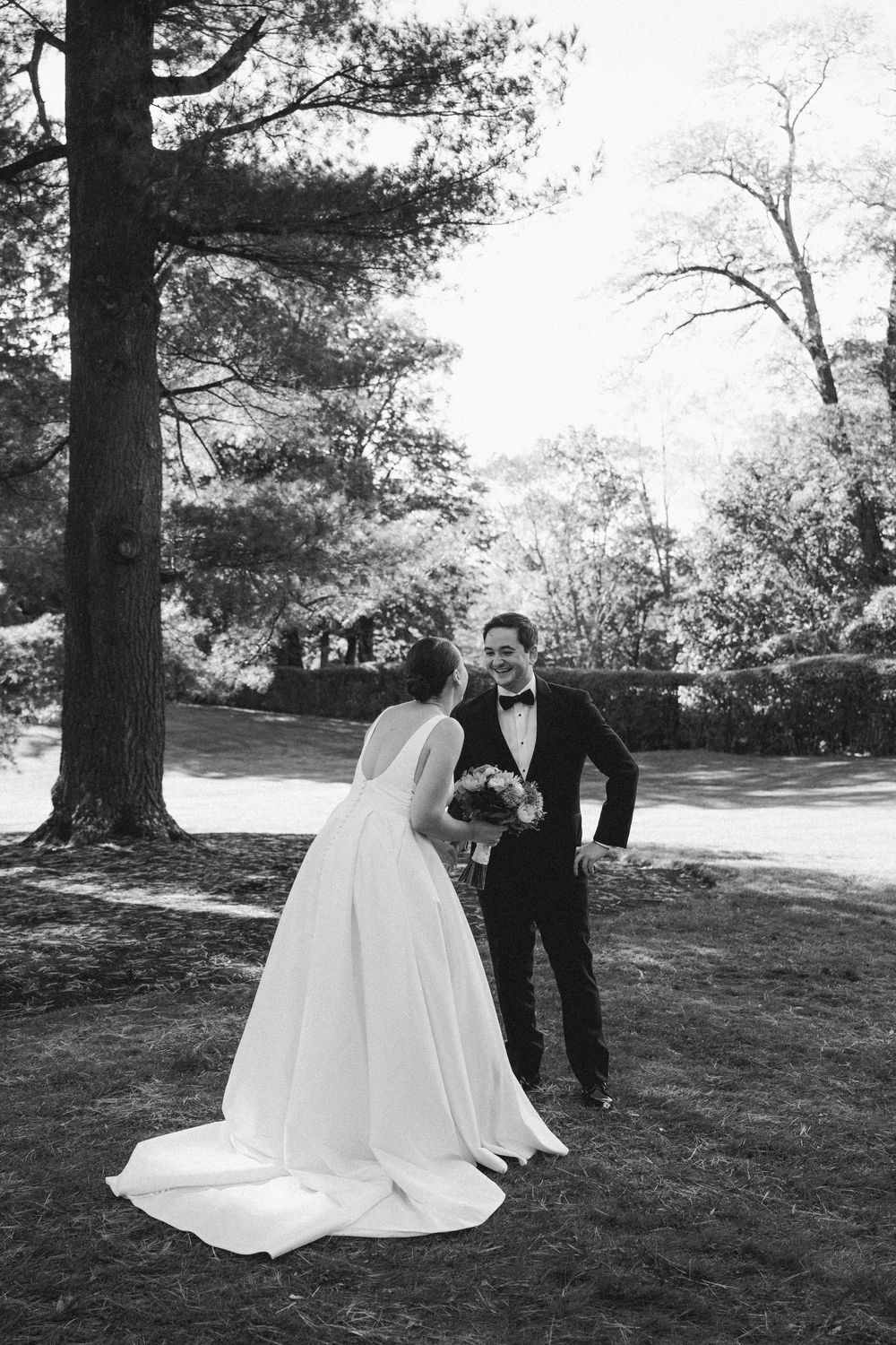 A bride in a flowing white gown and groom in a tuxedo share intimate moments during an outdoor photo session.