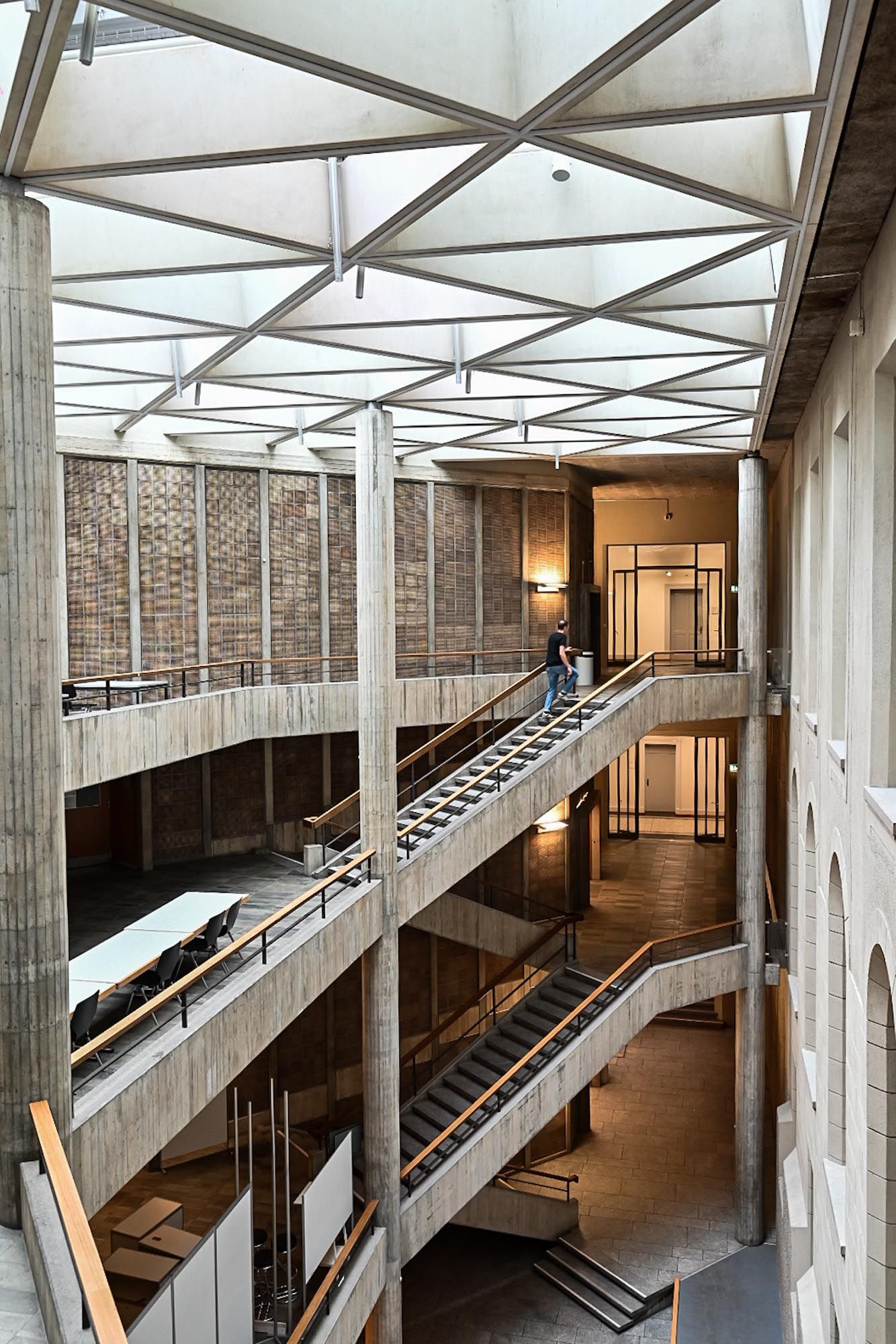 Modern architectural interior with concrete columns, diagonal staircases and skylights creating a geometric industrial space.