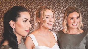 Three elegant women posing together at a wedding, wearing satin bridesmaid dresses with sophisticated hair and makeup.