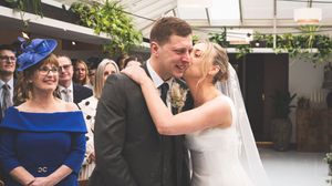A bride and groom share a joyful moment at their wedding ceremony with guests smiling behind them.