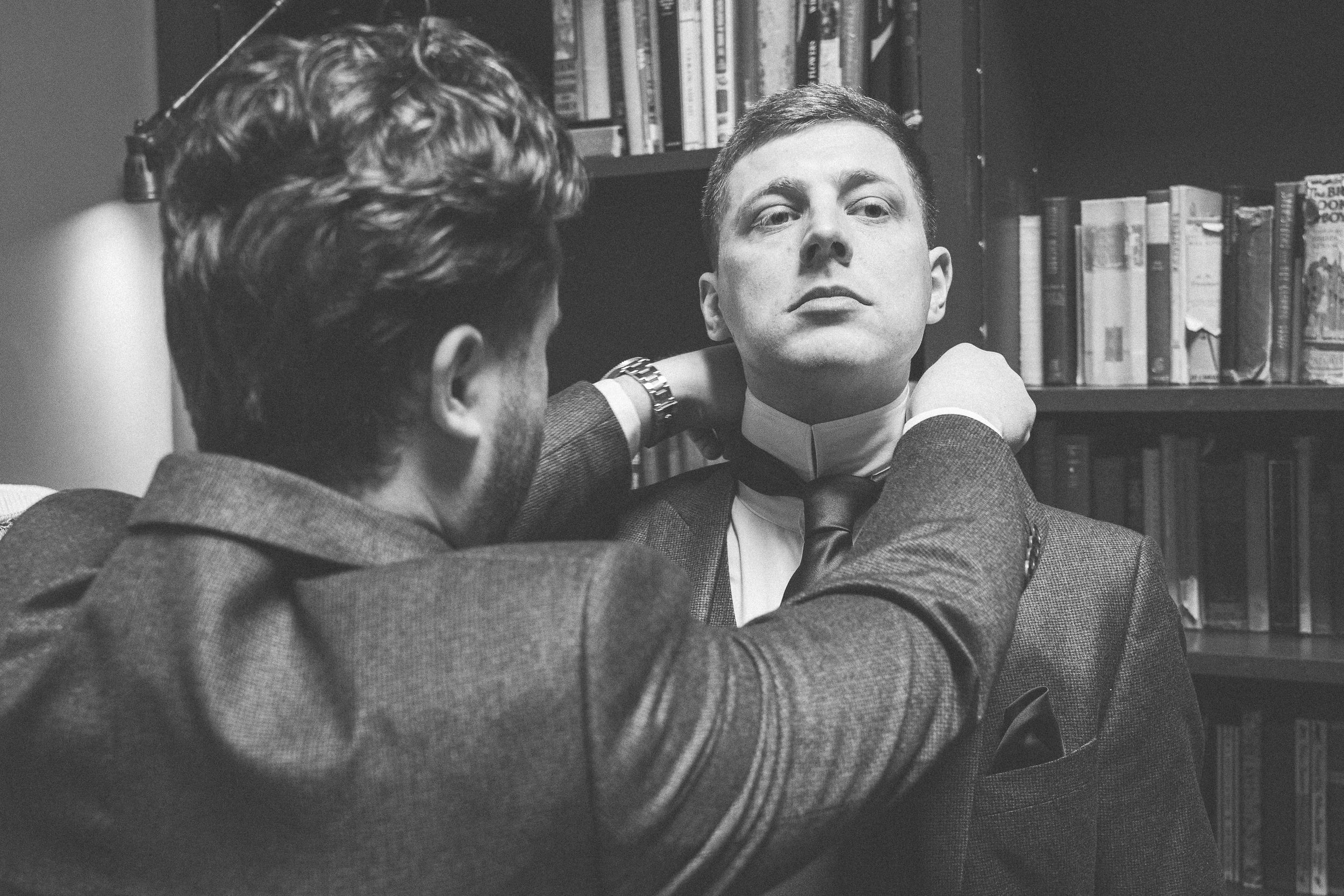 Black and white photo of a man adjusting another mans tie in a library setting.