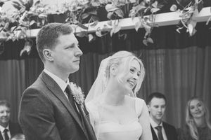 Black and white wedding photo showing couple dancing under string lights at outdoor reception venue.