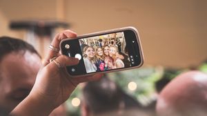 A smartphone held up in front of a blurred crowd displays a photo on its screen during an event.