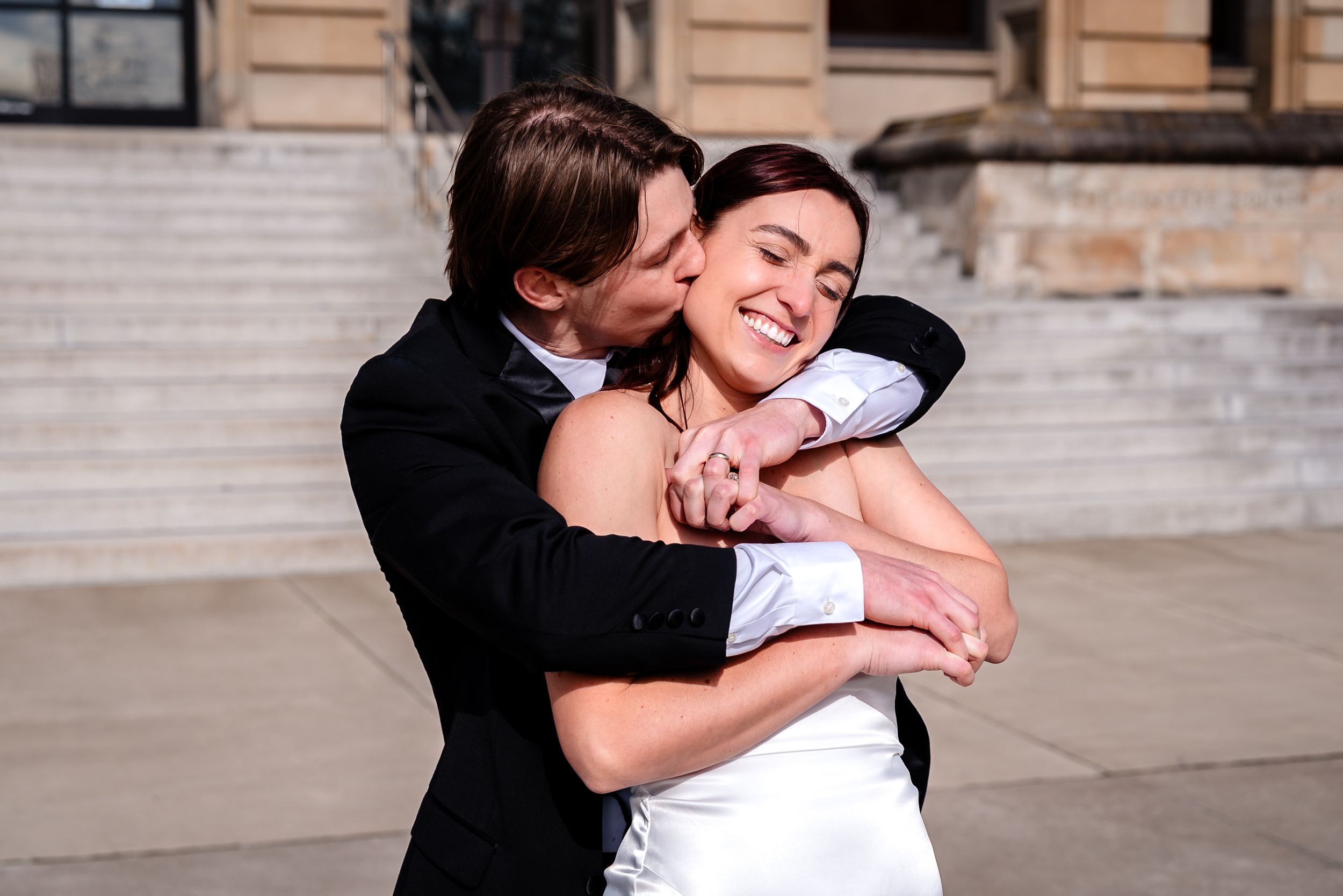A couple embraces and shares a tender moment in front of a stone building.