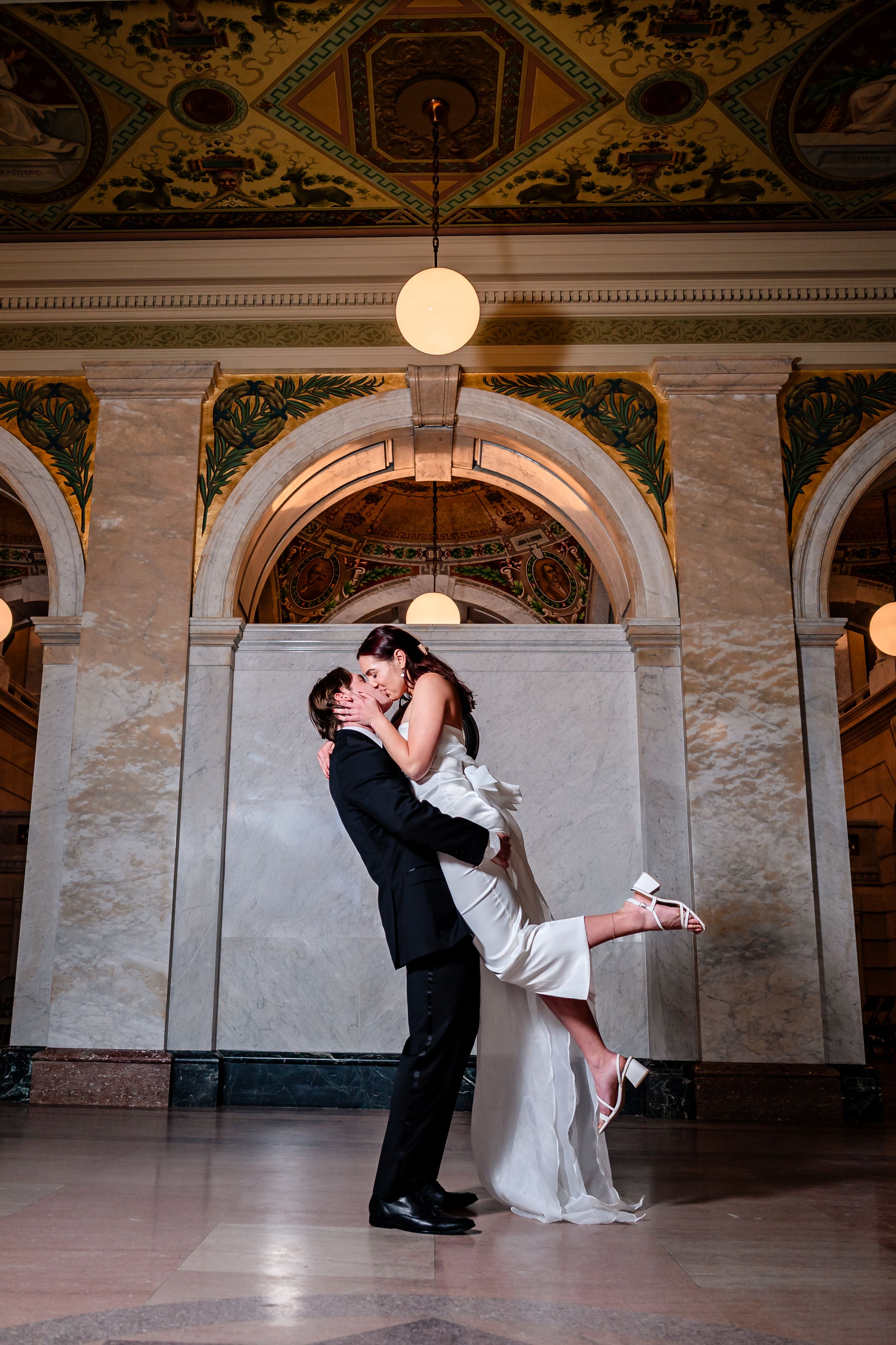 A romantic dance dip sequence in a grand ballroom with ornate architectural details and pendant lighting.
