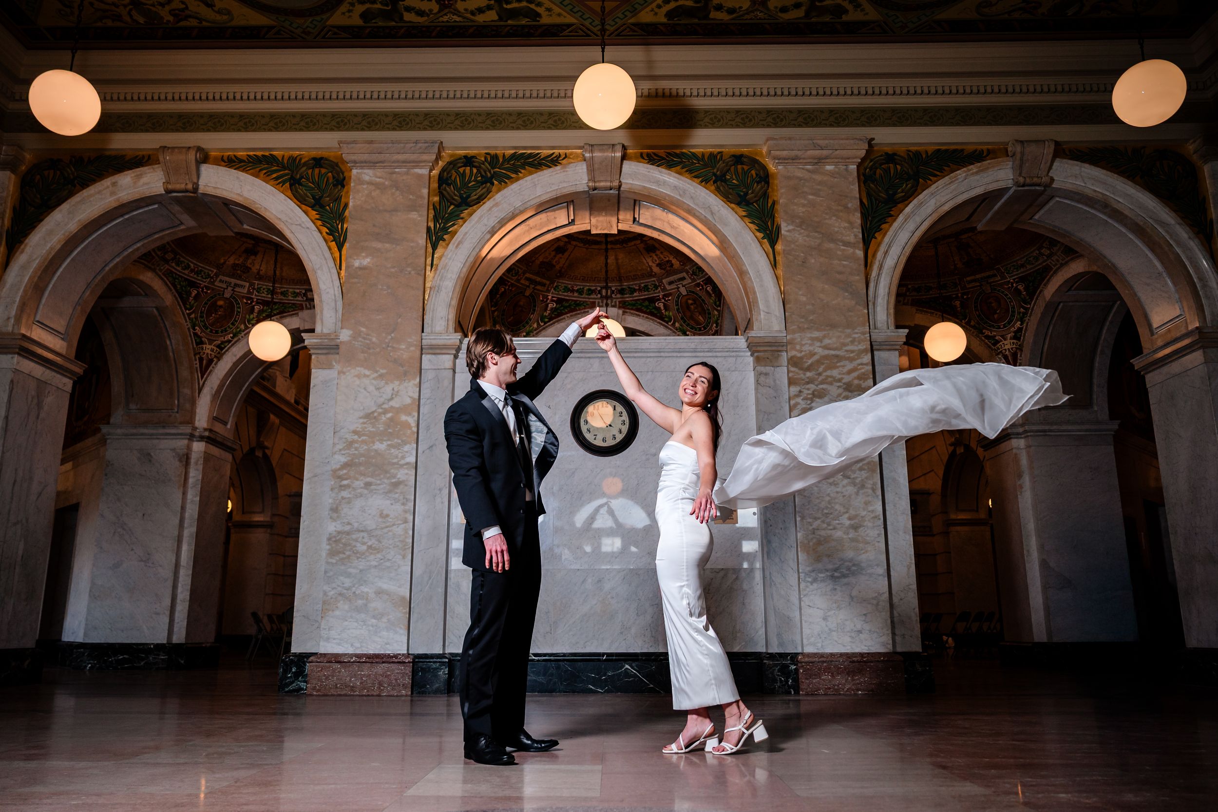 A couple shares a romantic moment under the arches of an elegant stone building with ornate architectural details.