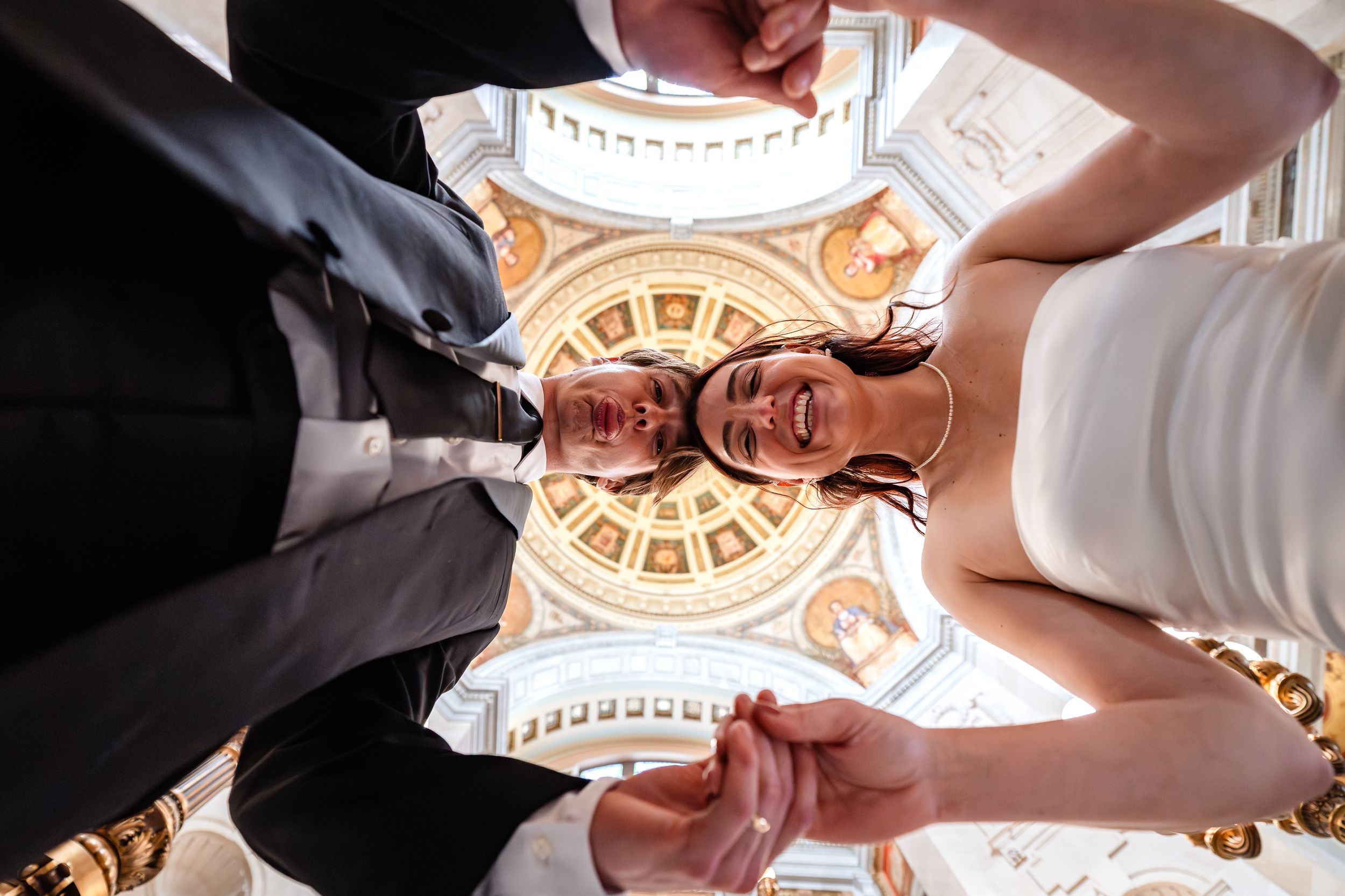 Looking up at ornate domed ceiling with decorative details and chandelier in classical architecture.