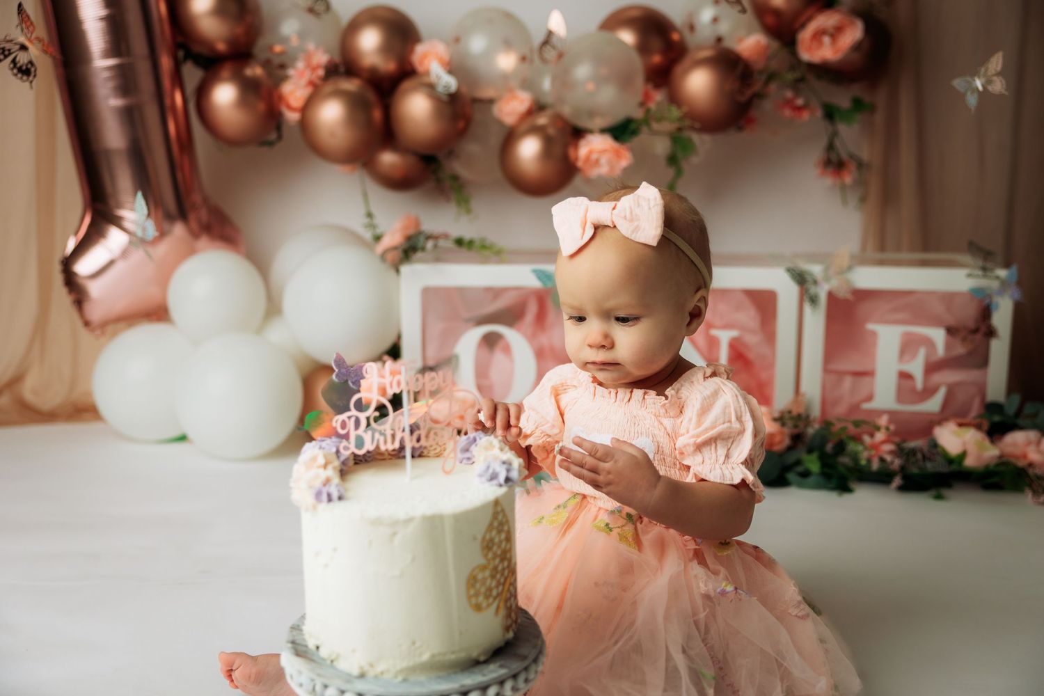 A baby in a gray romper sits with a smashed birthday cake and blue bunting decorations in the background.