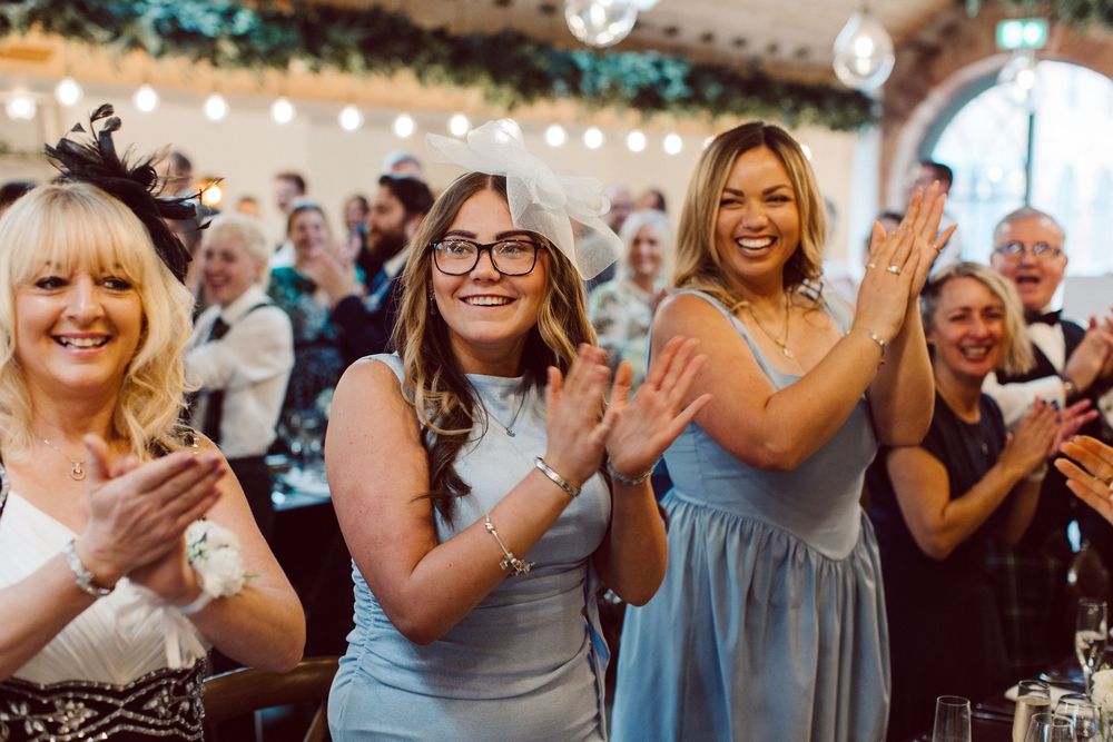 A group of wedding guests laughing and enjoying themselves at an outdoor reception with string lights overhead.