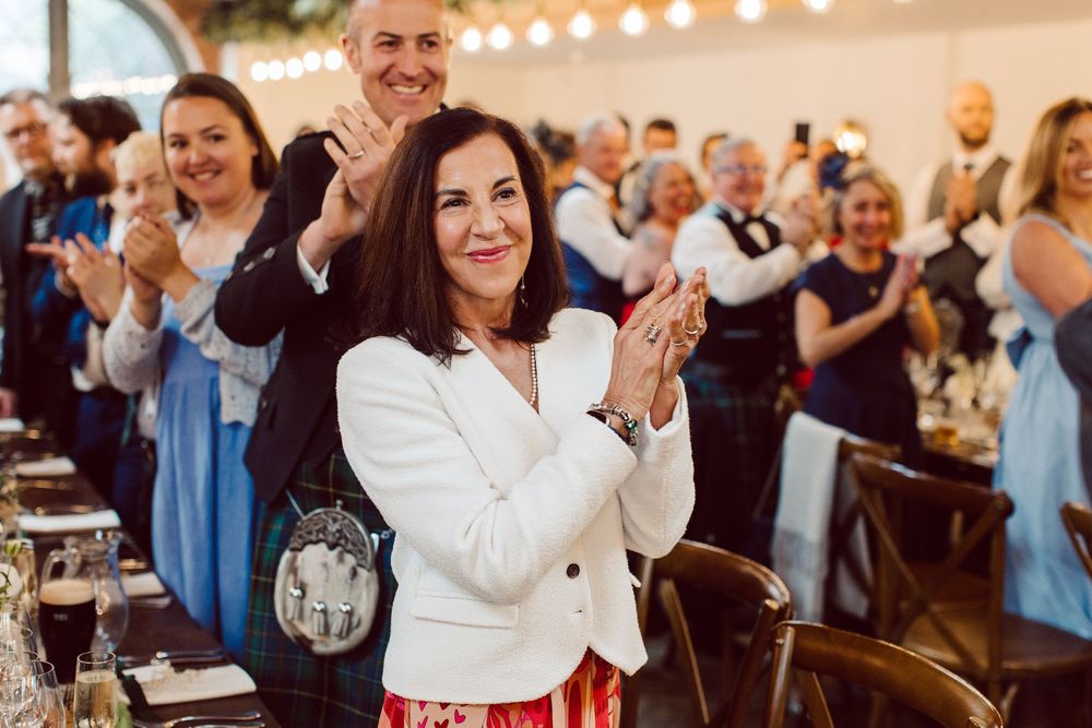 Wedding guests laugh and celebrate during a joyous reception with string lights overhead.