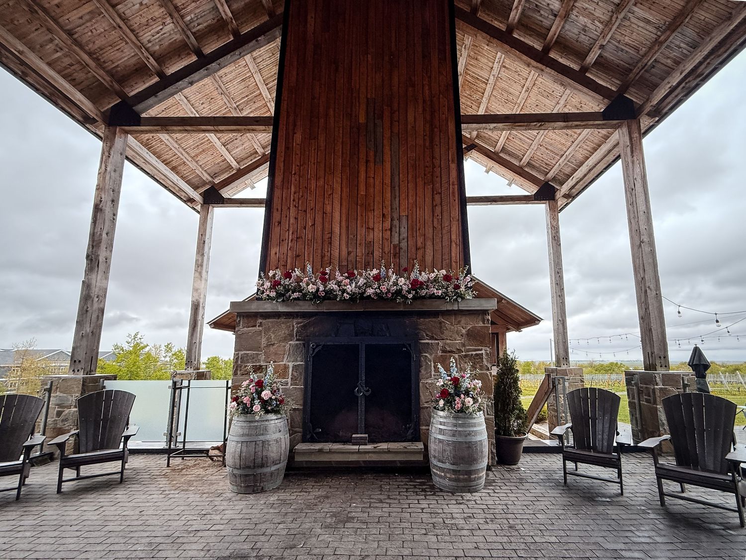 Rustic outdoor patio with stone fireplace, wooden beams, wine barrels and Adirondack chairs under covered pavilion at Lightfoot & Wolfville.
