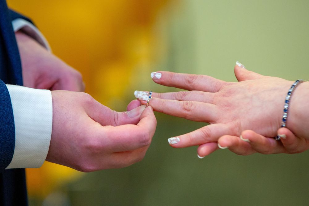 Groom places wedding ring on brides manicured hand with French tips during ring exchange ceremony.