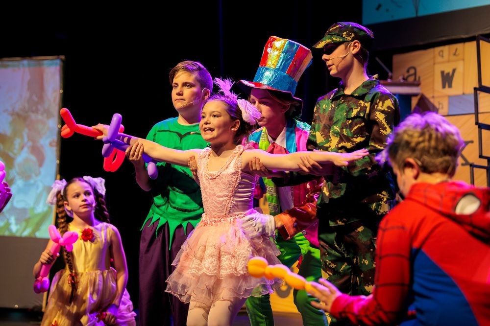 Children perform on a colorful stage in vibrant costumes during an energetic musical theater production.