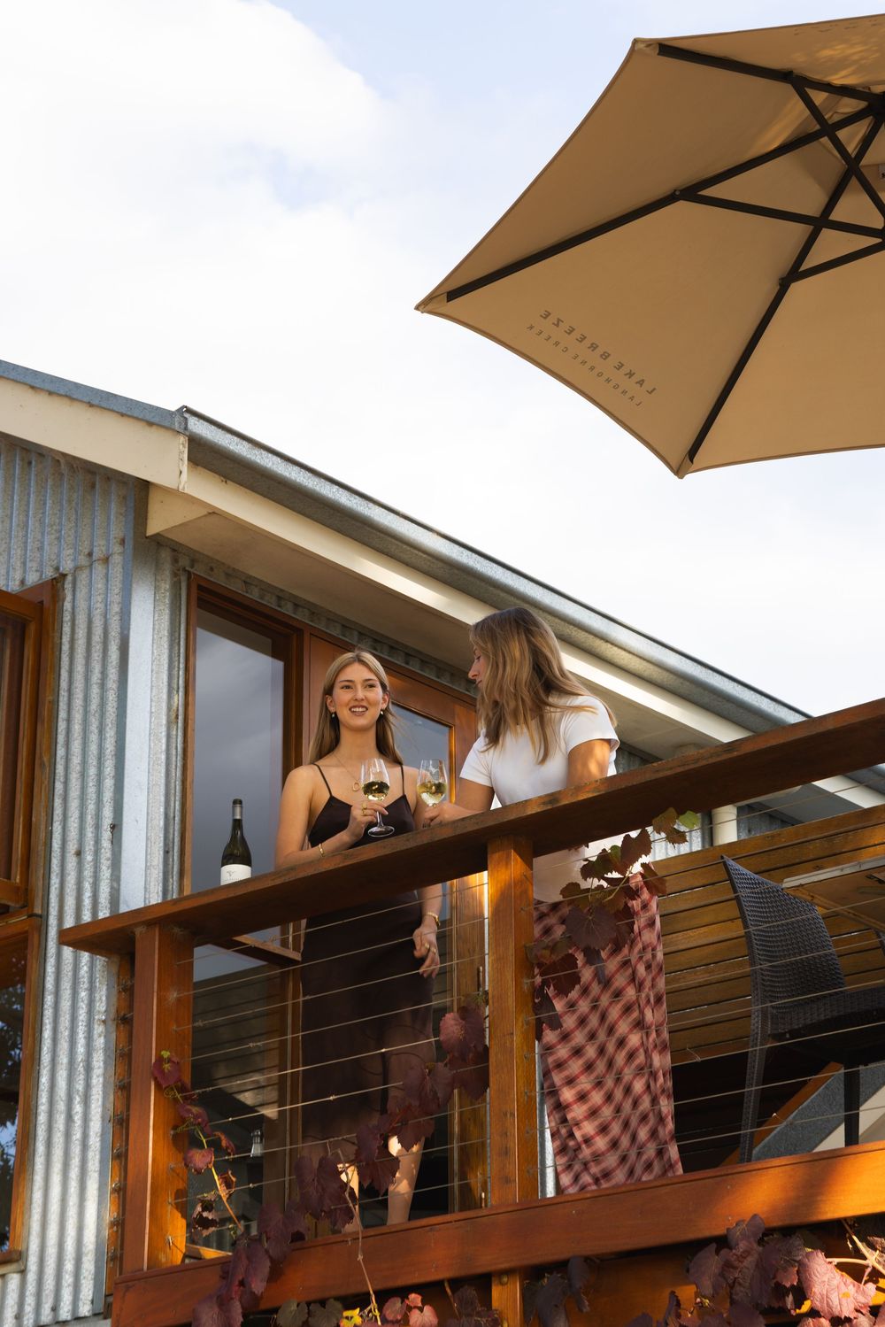 Two women enjoying wine on elevated winery balcony under umbrella