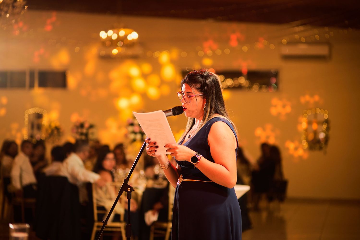 Wedding guests dance and celebrate on a dimly lit dance floor with warm amber lighting and chandeliers overhead.