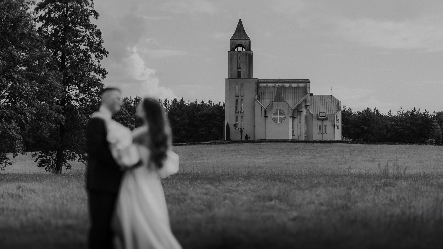Wedding couple silhouetted against sky with tree-lined path.