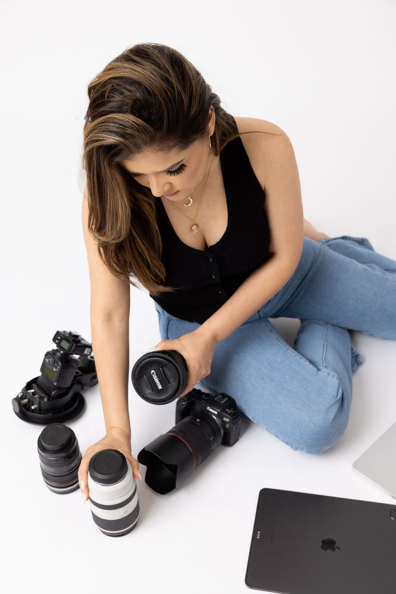 Person in blue jeans lying down with camera lenses and equipment on white background.