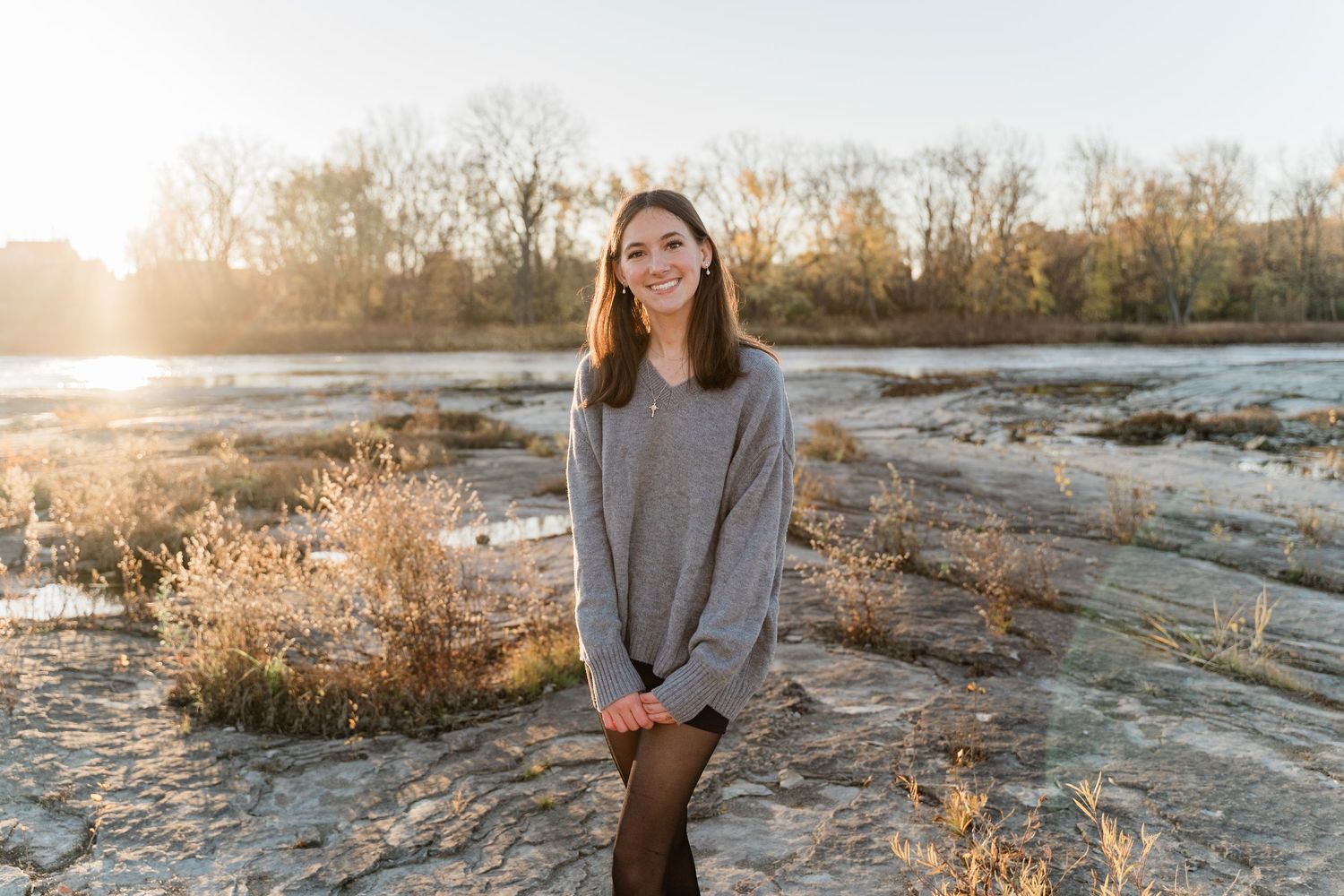 Toledo senior photo session in a gray sweater stands on rocky terrain at sunset with golden light illuminating the natural landscape.