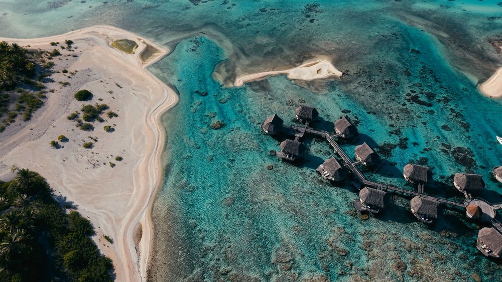 Aerial view of overwater bungalows and turquoise lagoon with white sandy beach in tropical paradise.
