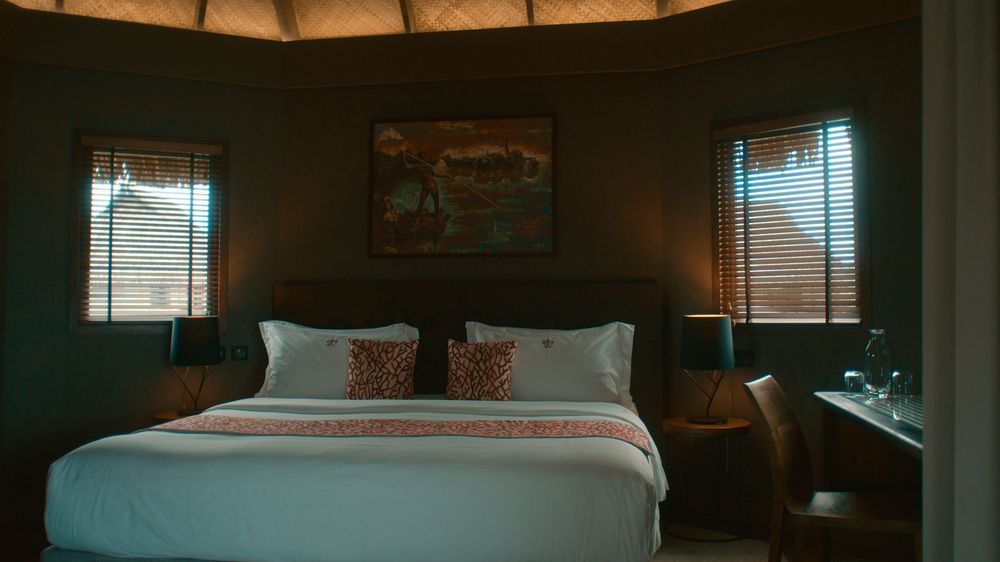 A panoramic view of a dimly lit bedroom interior with wooden blinds and natural light filtering through the windows.