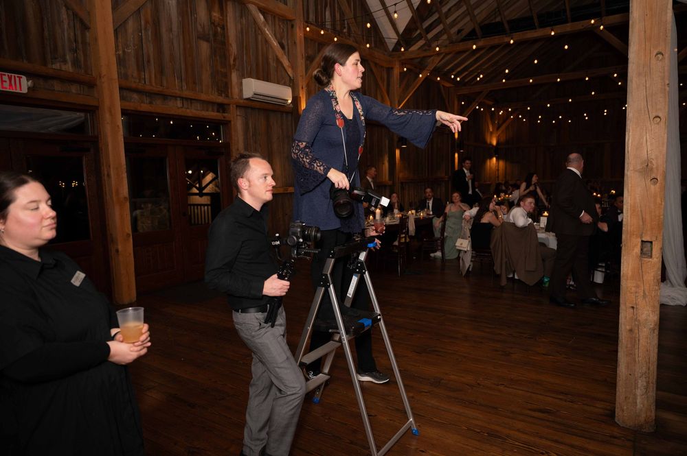 People dancing and celebrating at a rustic barn wedding reception with string lights and wooden beams overhead.