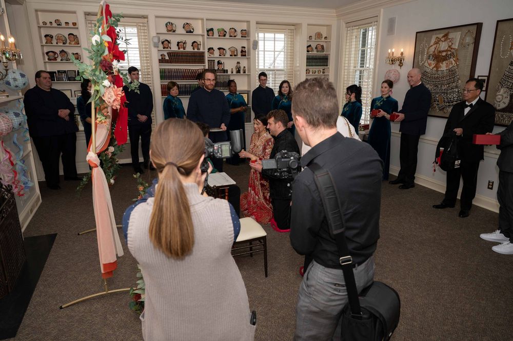 Wedding ceremony guests gather in a gallery space with artwork on walls and red decorative elements.