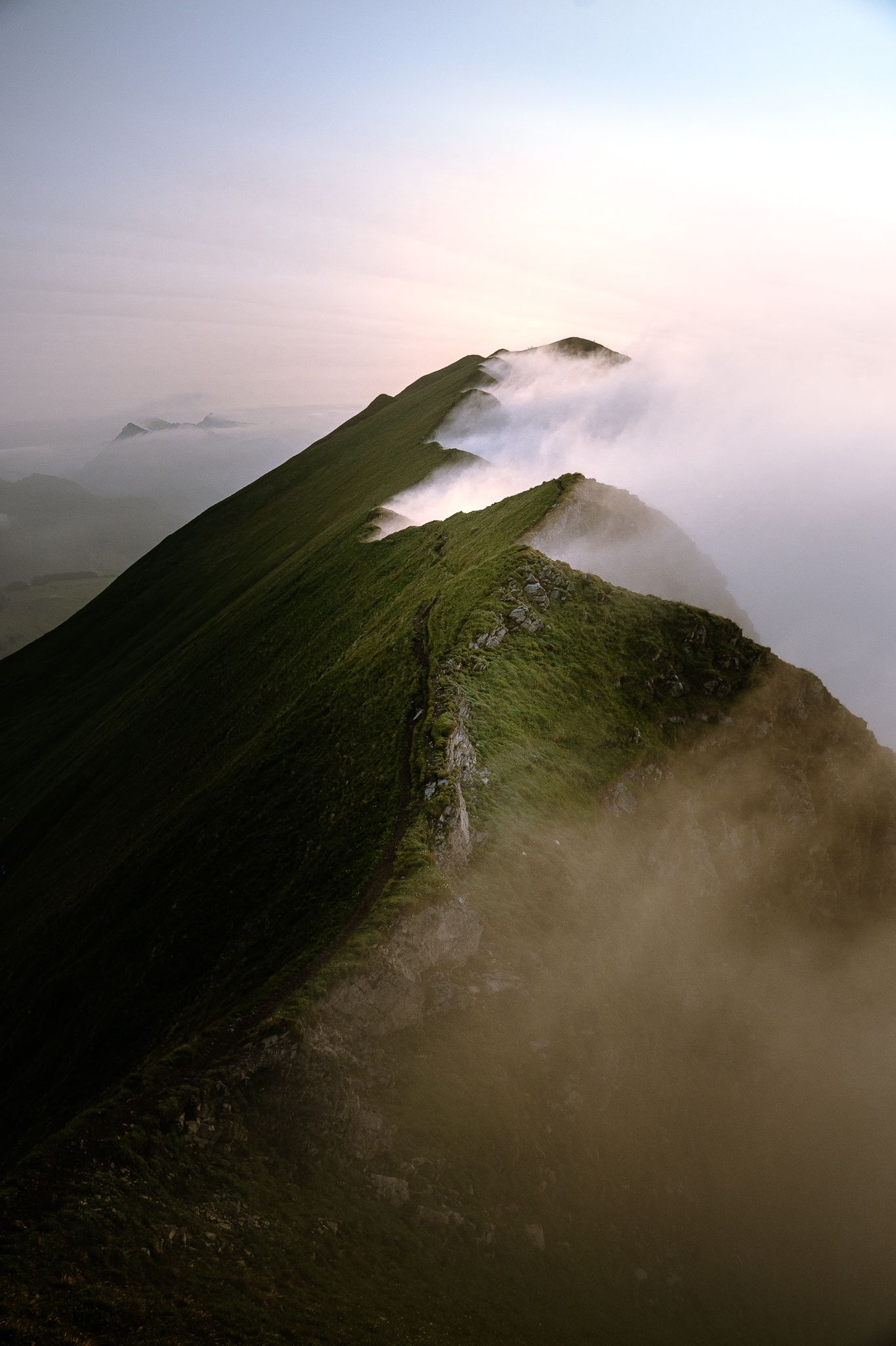 Aerial view of a green mountain ridge emerging through dramatic clouds at sunset.