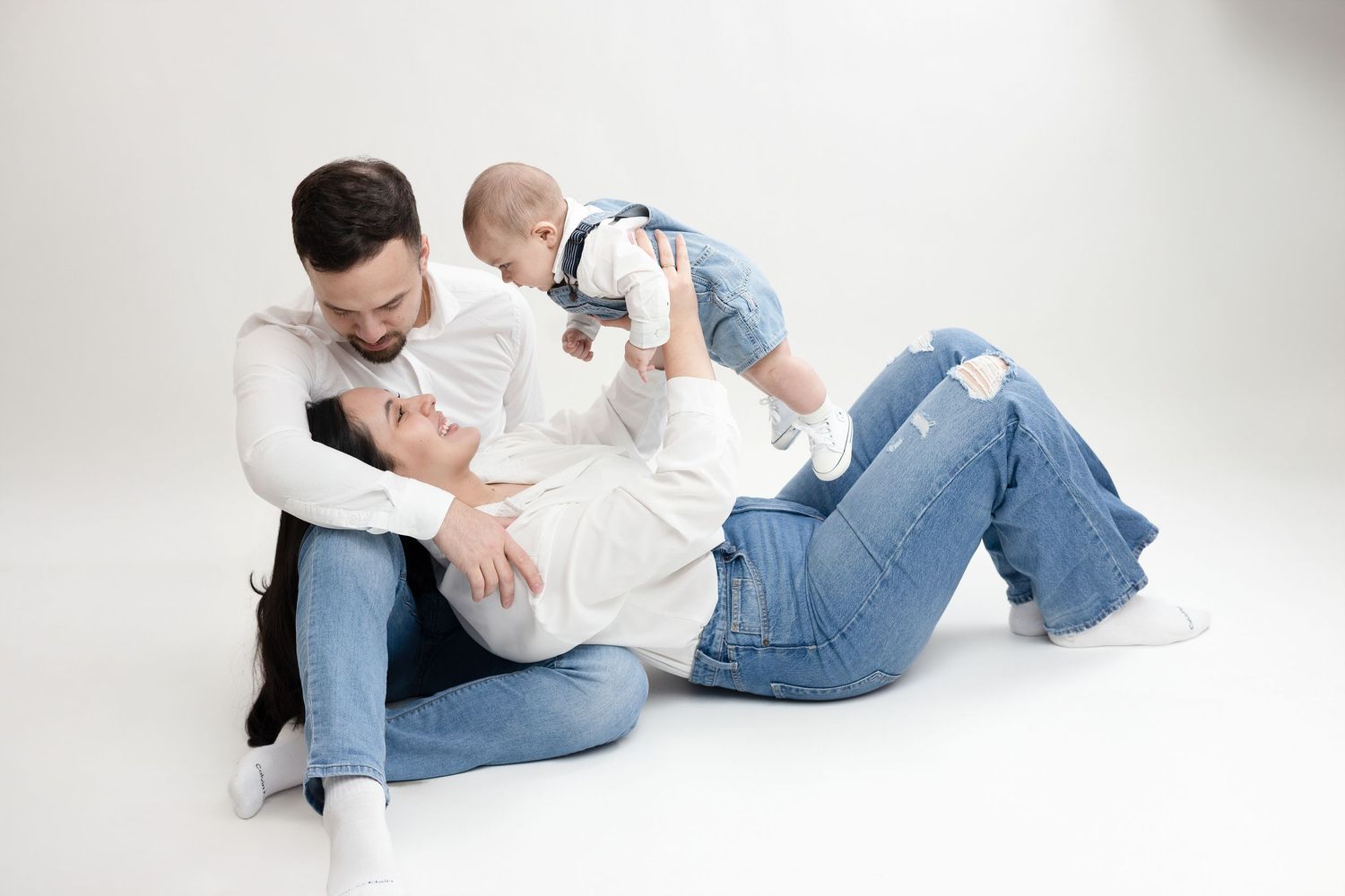 A family in casual denim outfits plays together on a white backdrop during a studio photo session.