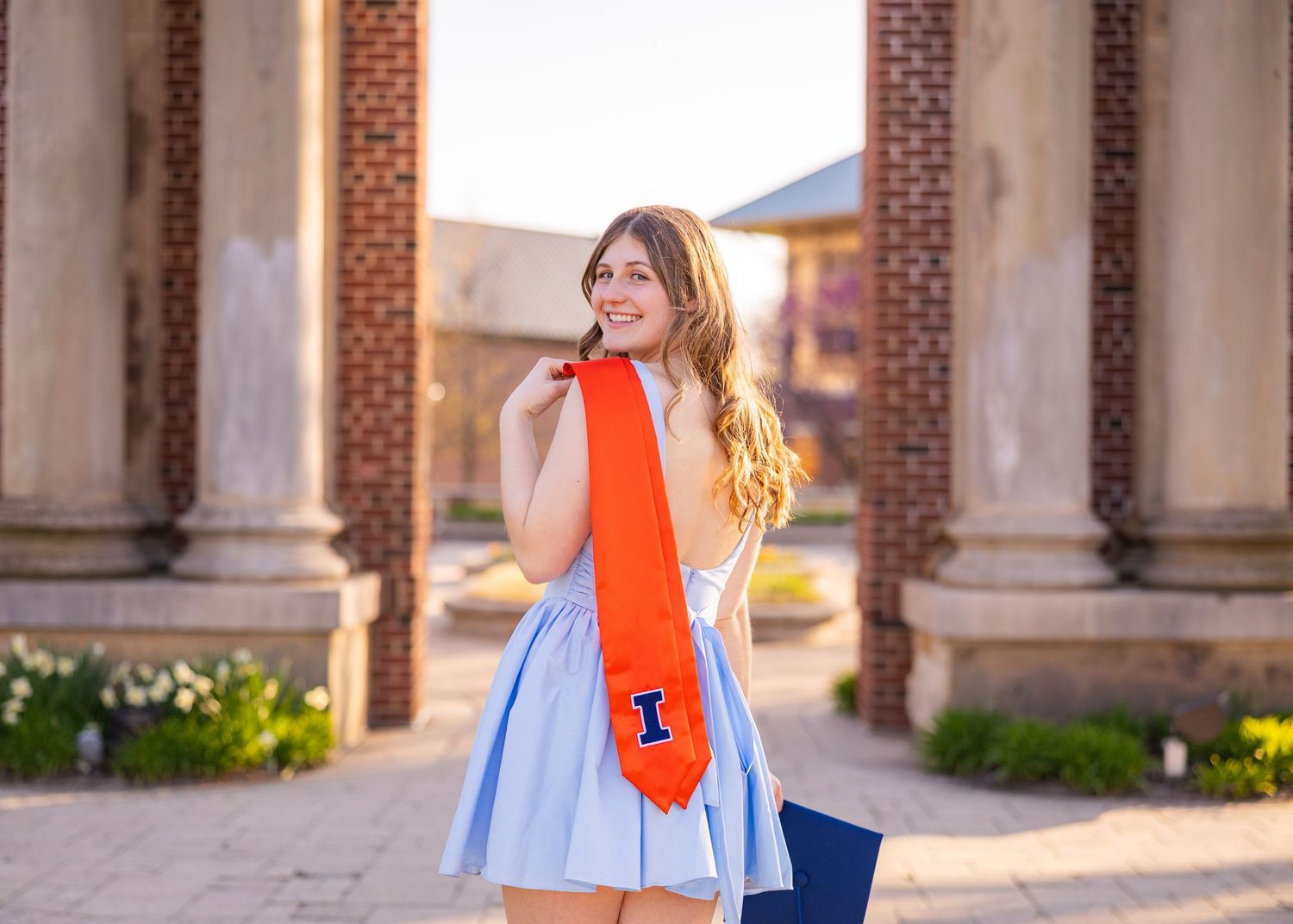 Girl in blue dress holding a UIUC stole over her shoulder at Hallene Gateway