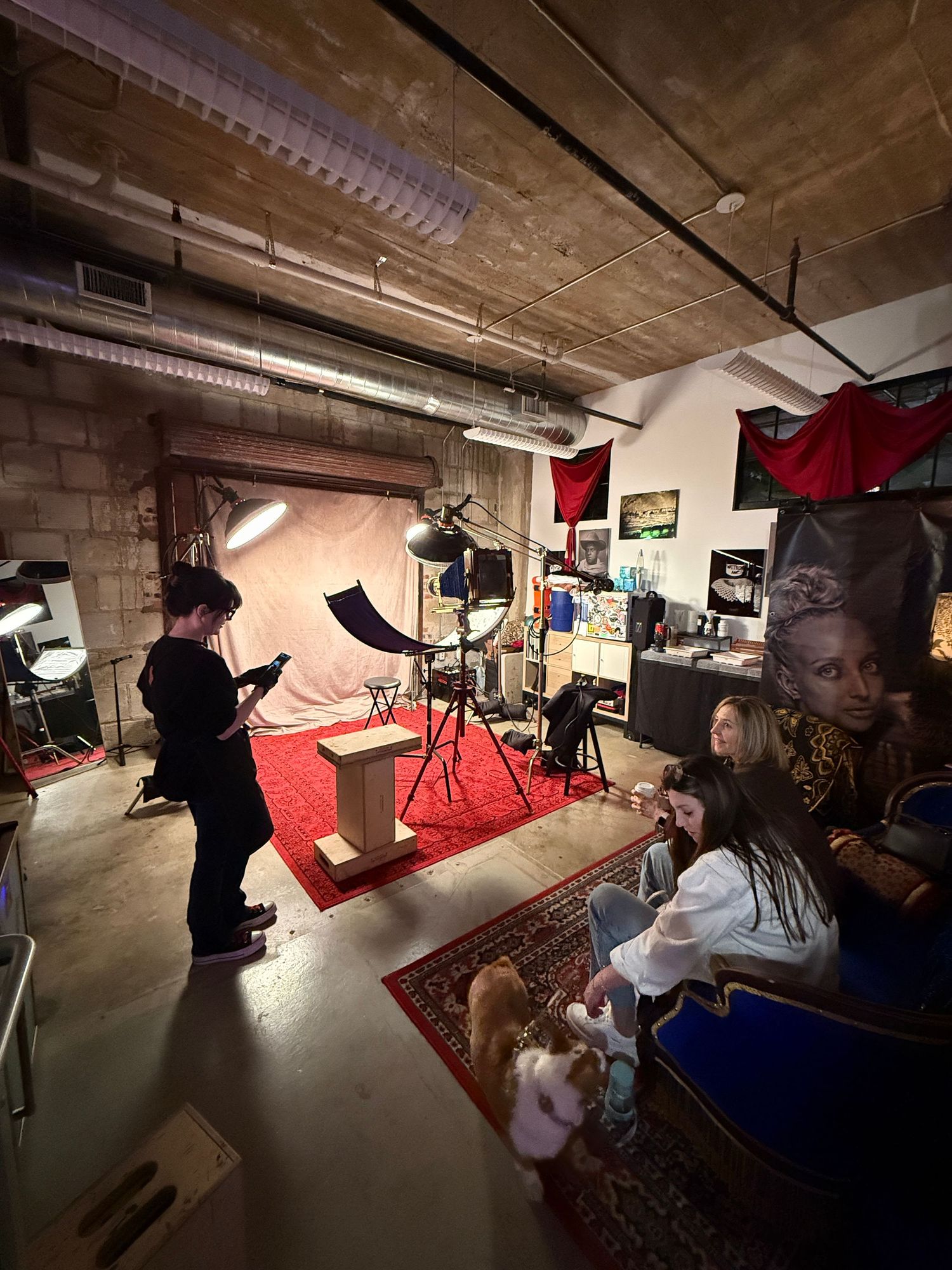 Film production crew working on set with lighting equipment and red backdrop in a studio space.