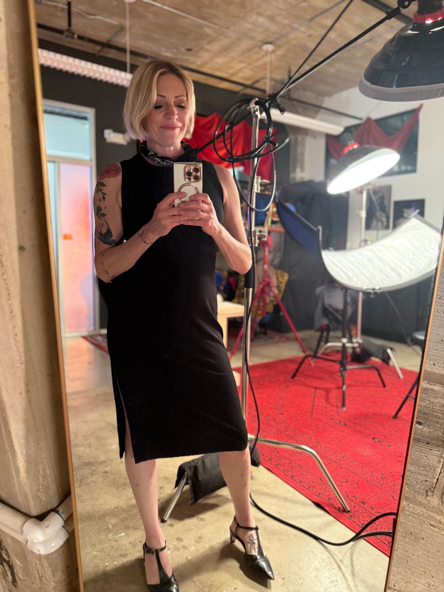 Person in black attire stands in a studio space with red carpet and professional lighting equipment.