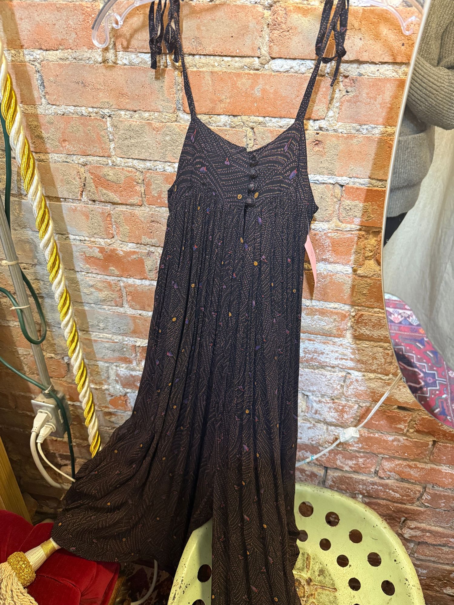 A navy blue sleeveless dress with pleated details hangs on a clothing rack against a rustic brick wall.