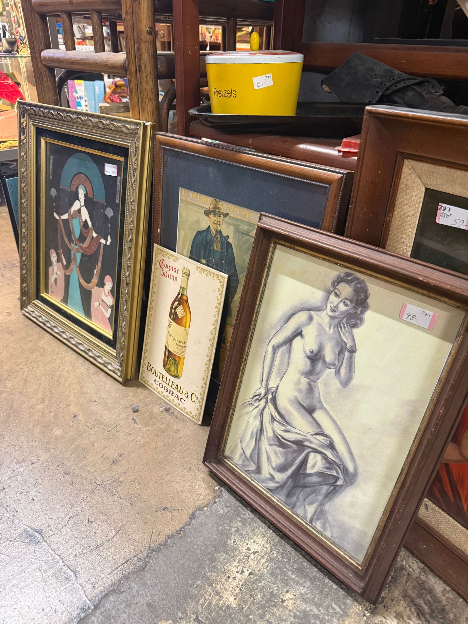 A collection of vintage framed photographs and artwork displayed on wooden shelves in an antique store setting.