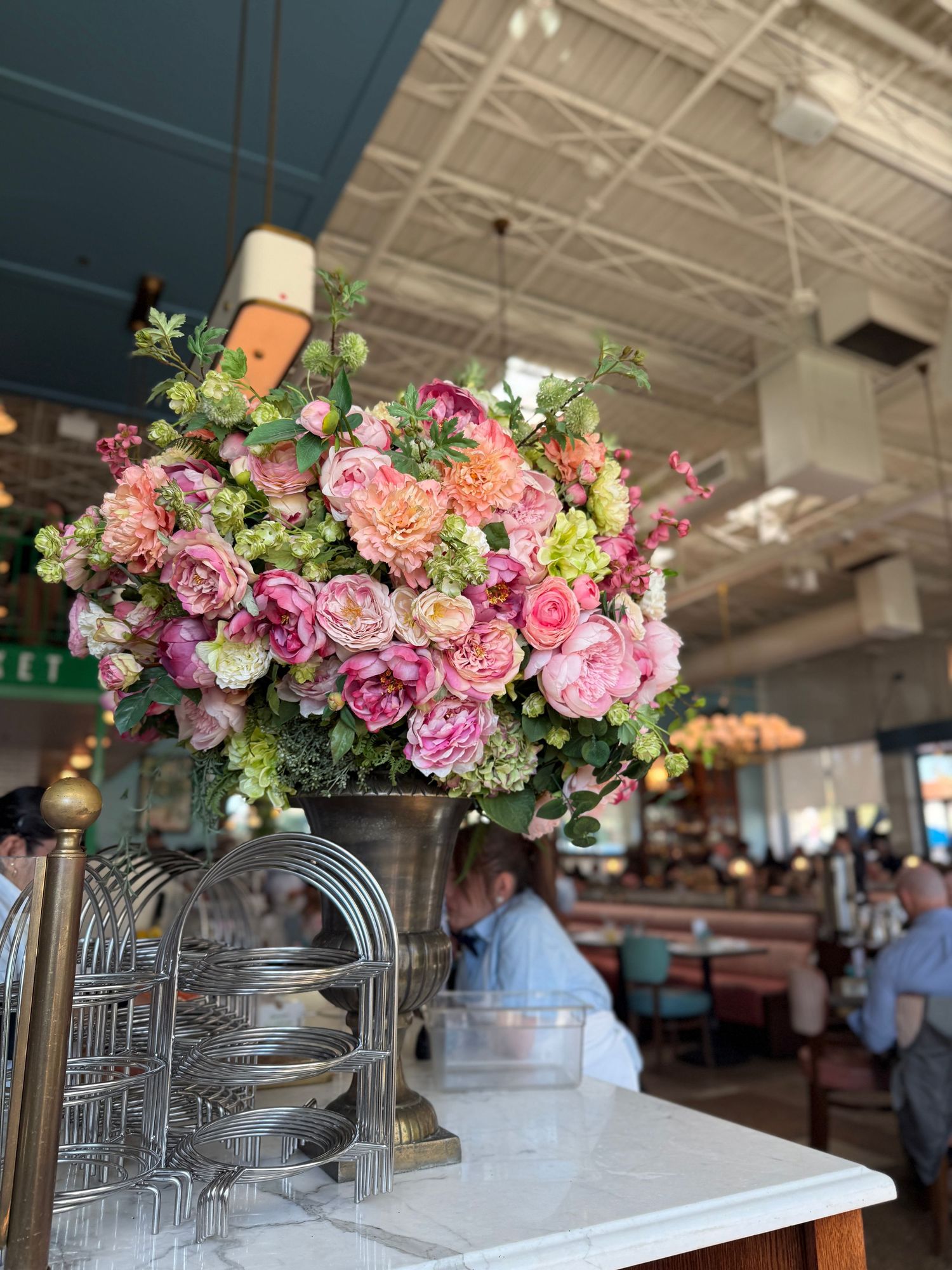 Elegant floral centerpiece arrangement with pink and purple blooms displayed on white marble counter in restaurant setting.