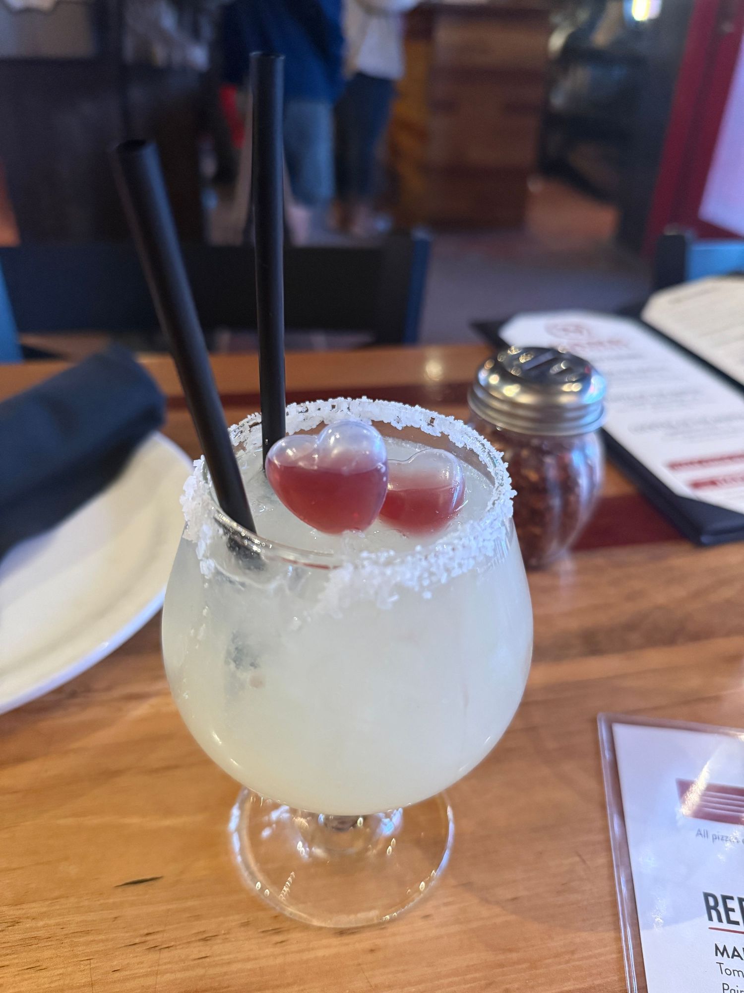 A line of margarita cocktails with salt rims and fresh garnishes sit on a wooden bar top.