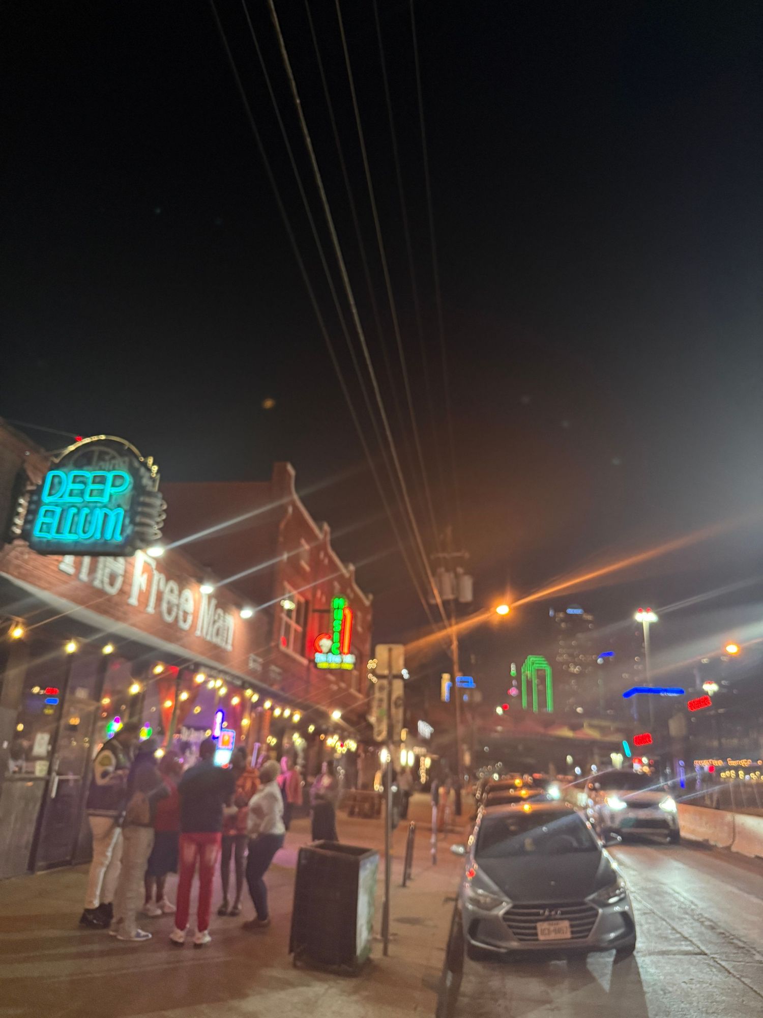 A nighttime street scene shows illuminated business signs and storefronts with people gathered on the sidewalk.