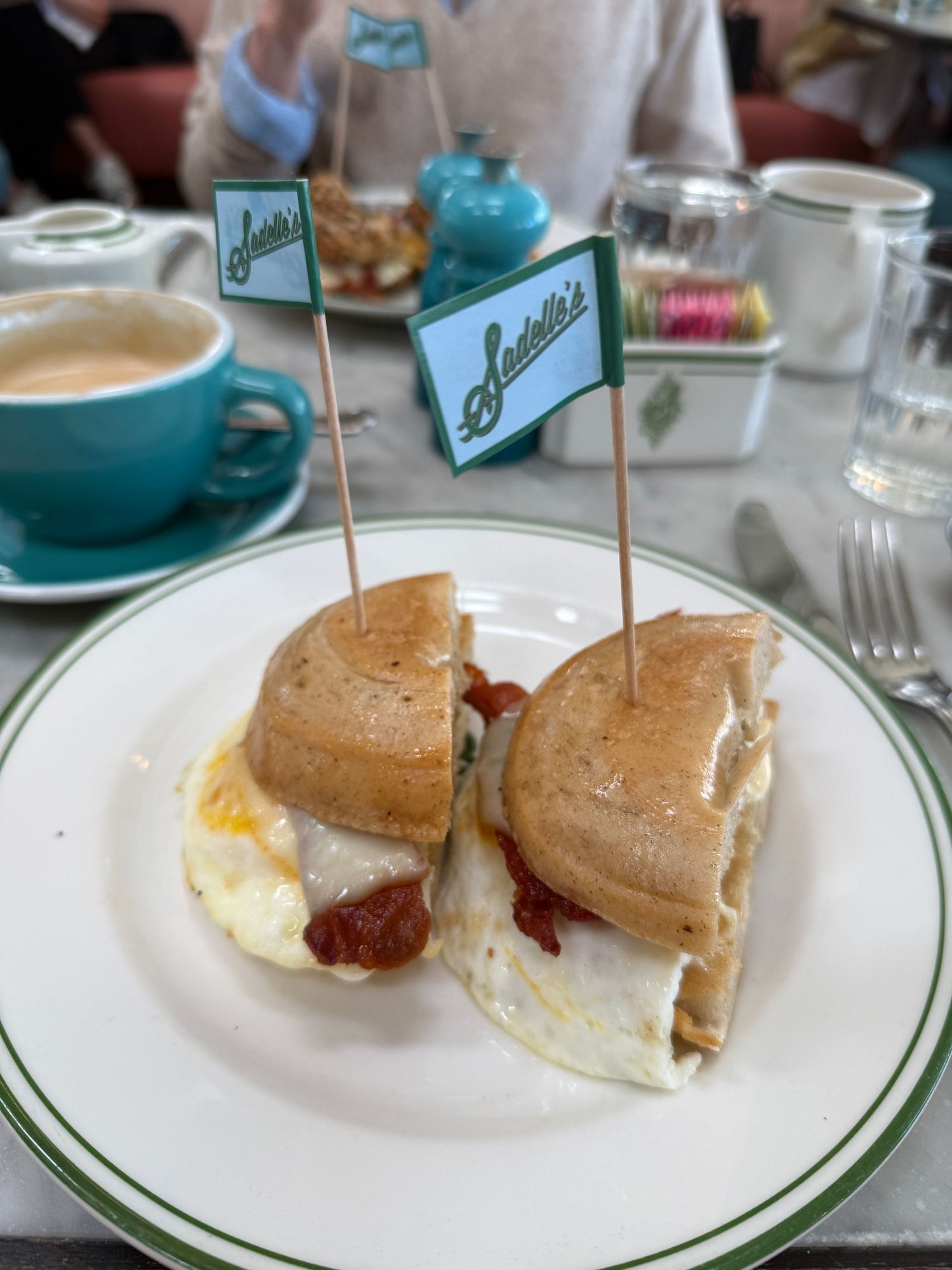A plate of biscuits with butter and jam served at a restaurant with green trim on white plates.