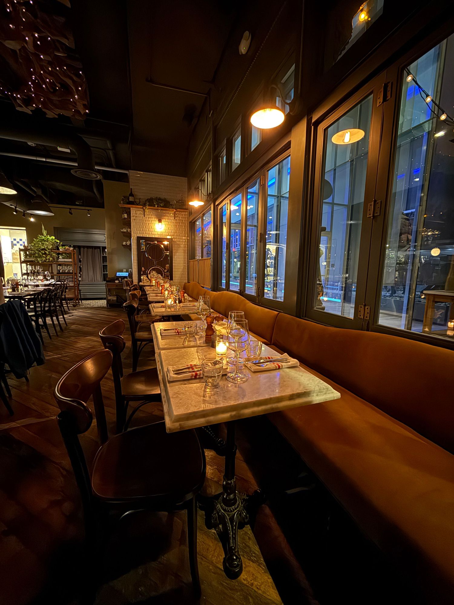 A dimly lit restaurant interior with wooden tables, bench seating, and warm ambient lighting creating a cozy atmosphere.