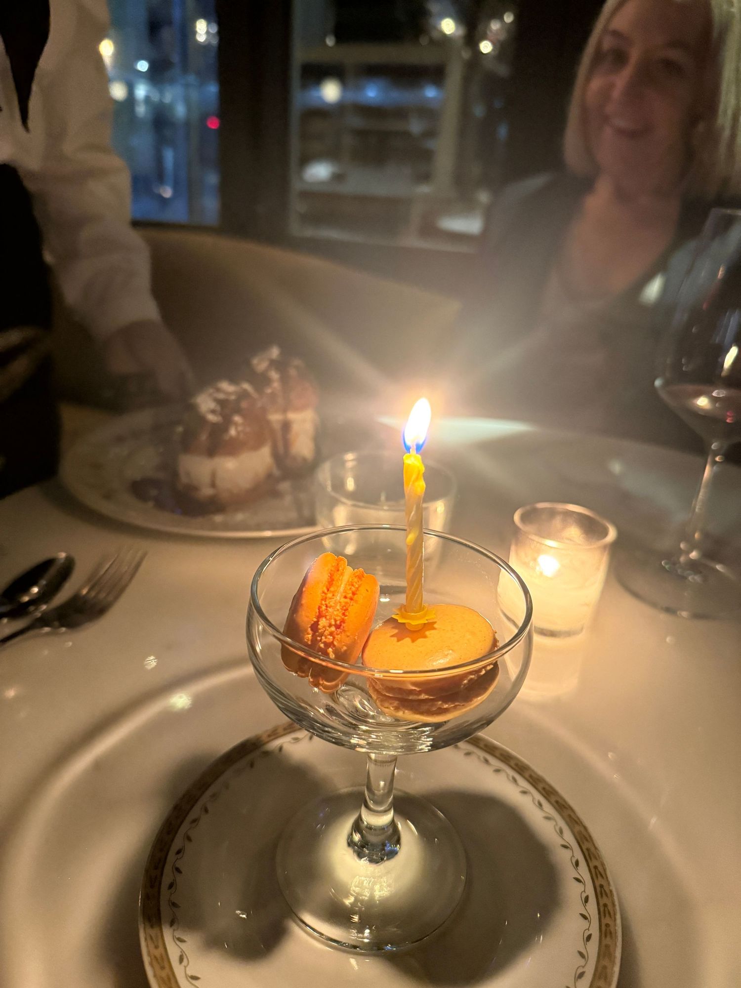 Cocktail glass with a lit birthday candle in a dimly lit restaurant setting.