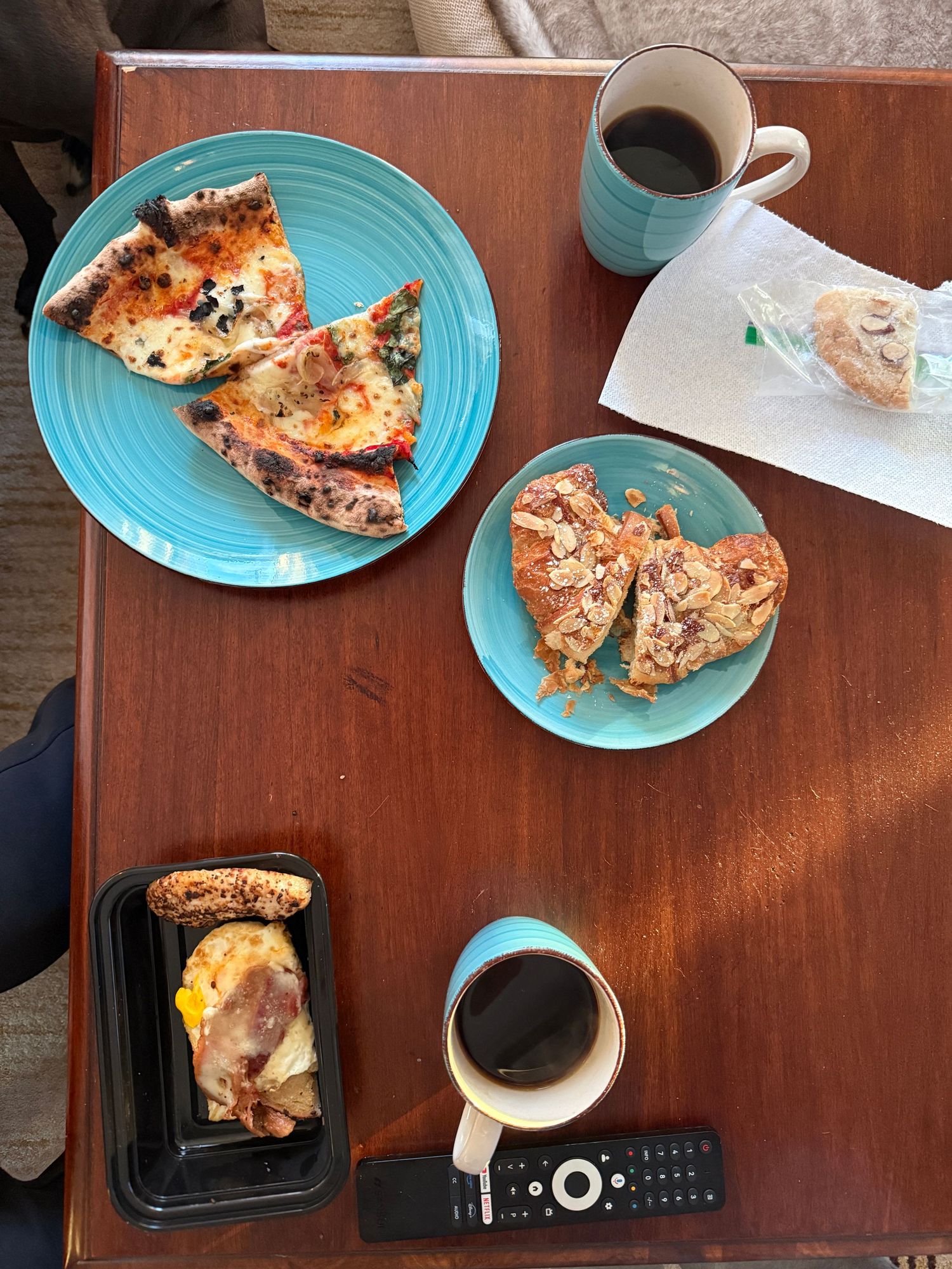 Breakfast spread on turquoise plates featuring toast and sandwiches with coffee mugs on a wooden table with a TV remote.