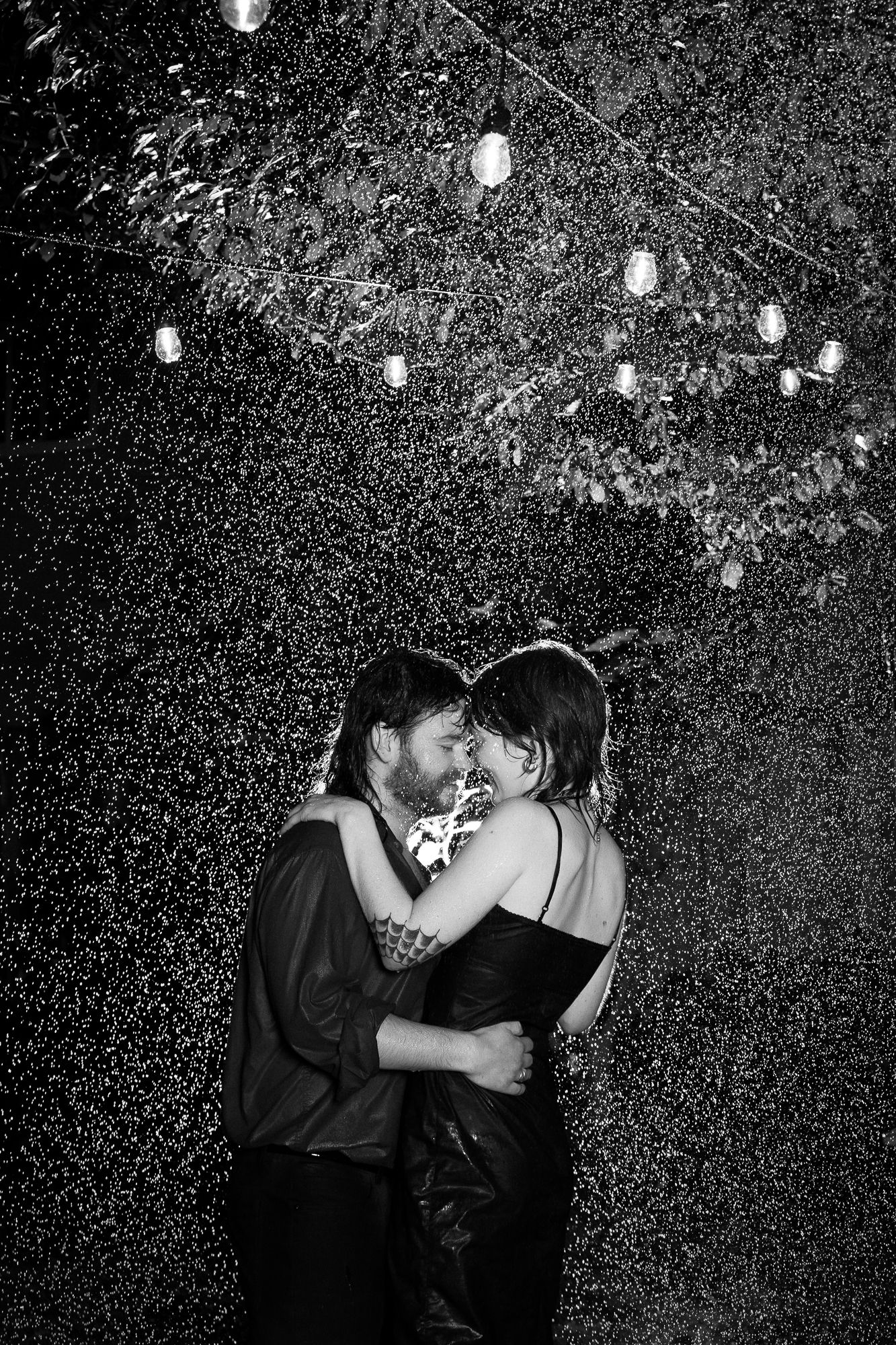A man and woman are holding each other in the rain. They are backlit, so you can see every last raindrop showering them.