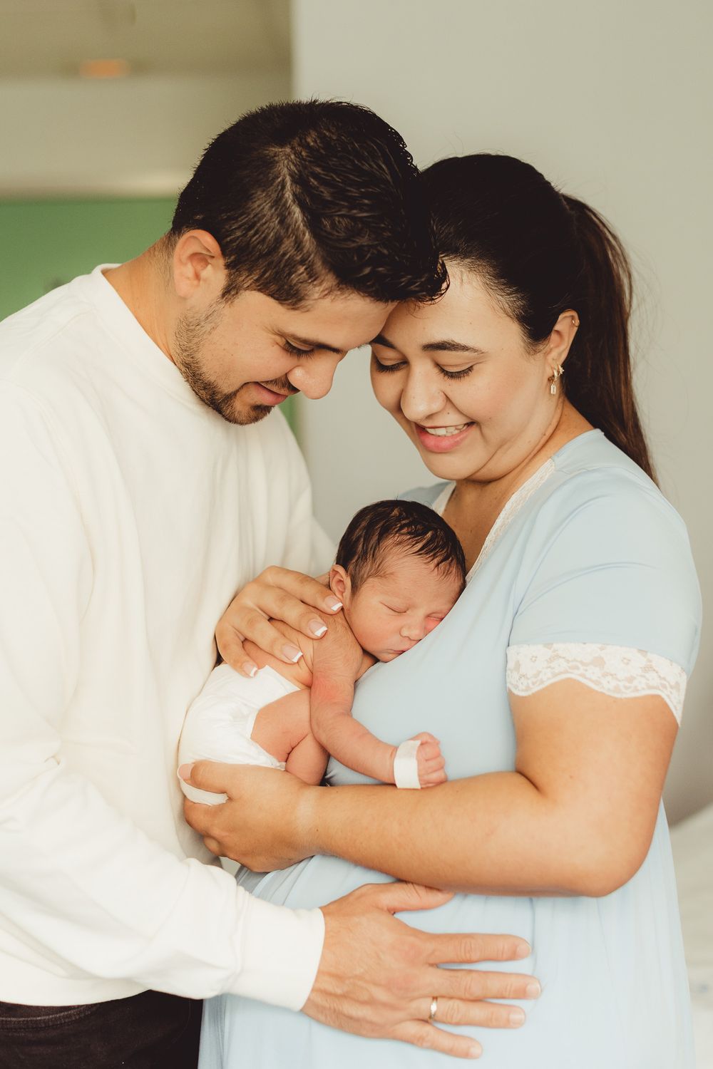 New parents tenderly hold their sleeping newborn baby, touching foreheads in an intimate family portrait.